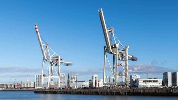 Wide view of shipping cranes against Hamburg skyline under clear blue sky.