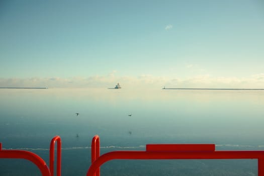 Calm ocean scene with a distant ship and red barrier in foreground.
