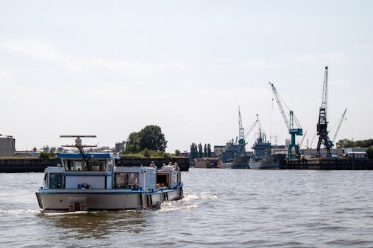 Ghidul Complet al Carierei de Marinar în 2026: Certificări STCW, Training Maritim și Simulare Avansată 3 A lively harbor scene in Hamburg with a boat sailing and construction cranes in the background.