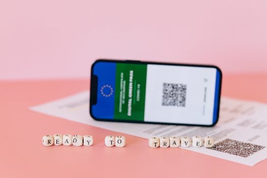 Smartphone displaying digital green pass on a pink surface with travel beads.