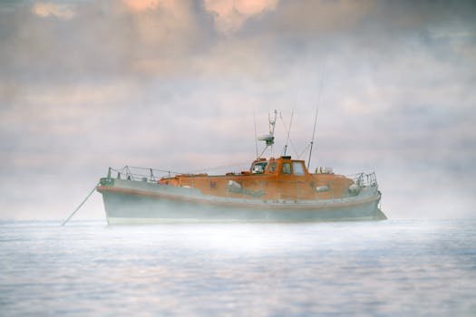 A lone orange lifeboat drifts in a serene, misty seascape at sunrise.