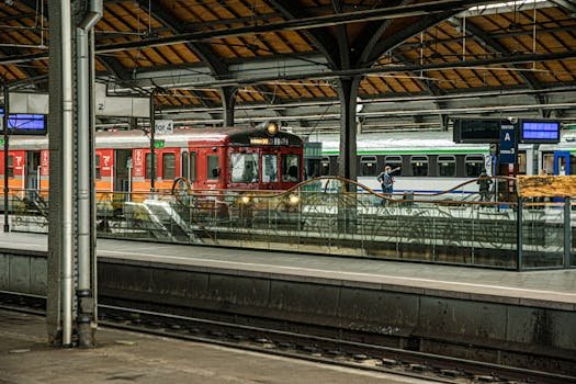 Historic red train at bustling urban station platform with glass barriers and commuters.
