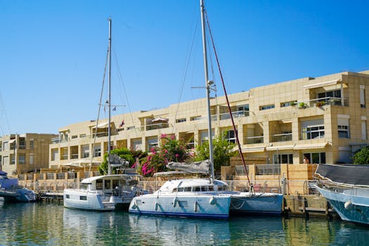 Beautiful Herzliya Marina in Tel Aviv District with modern apartments and anchored sailboats under a clear blue sky.