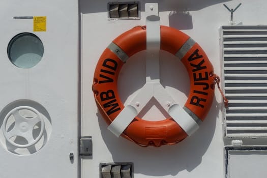 Viața la Bord în 2026: Sfaturi Esențiale, Cursuri Online de TOP și Joburi Căutate pentru Navigatori! 2 Close-up of a lifebuoy on a ship's white wall with Rijeka text, in bright daylight.