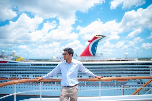 A man in sunglasses and white shirt enjoys a sunny day on a cruise ship deck with puffy clouds overhead.