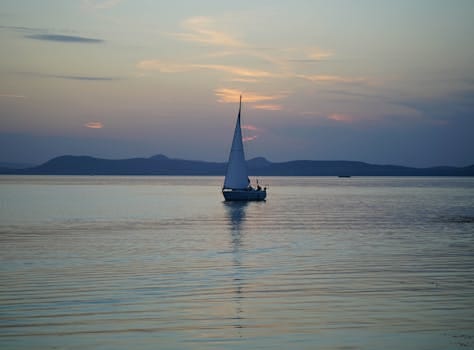A sailboat glides across Lake Balaton in Hungary during a serene sunset, reflecting tranquility.
