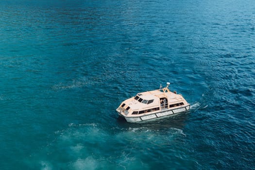 Ghid complet pentru obținerea certificatului STCW: pași și avantaje 2 Serene aerial view of a small boat cruising through clear blue ocean waters.
