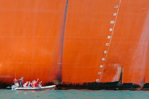 Inflatable boat with people in red vests near a large cargo ship hull.