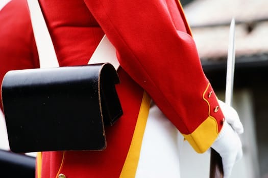 Detail view of a red historical military uniform with a black leather pouch and white glove.