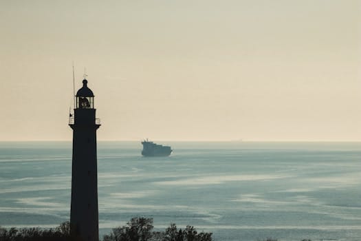 A serene view of a lighthouse against the Dardanelles Strait at Çanakkale, Türkiye, with a ship on the horizon.