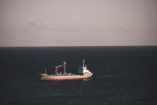 A lone cargo ship cruising through the vast and tranquil open sea under a pastel sky.