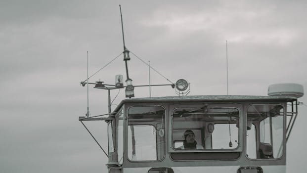 Cum să te Pregătești Eficient pentru Testul de Marinar Calificat pe Petrolier 4 A captain stands on the bridge of a ship, navigating through cloudy weather.