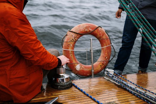 Close-up of two men navigating a sailboat, emphasizing safety with a lifebuoy at sea.