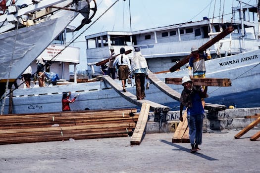 Indonesian workers loading timber onto ships at a bustling port, showcasing maritime and labor activities.