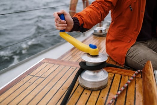 Pași pentru a Obține Certificat Marinar Vreme Rea și Sfaturi de Pregătire 2 Man in orange jacket operating winch on sailboat deck during daytime sailing adventure.