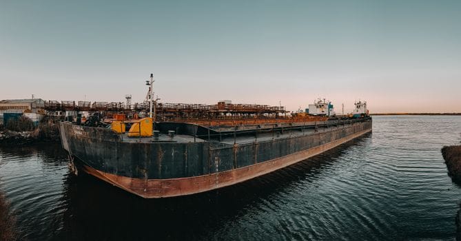Cum să Alegi Echipament Siguranță Maritim Reglementat pentru Navigație Oceanică 3 A large cargo barge docked at an industrial harbor during sunset, calm waters and clear sky.