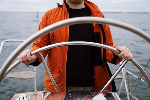 Cum să Alegi un Curs Maritim Distanță Acreditat: Tutorial Detaliat pentru Navigatorii Români 2 Close-up of a captain steering a boat in the sea, wearing an orange jacket.