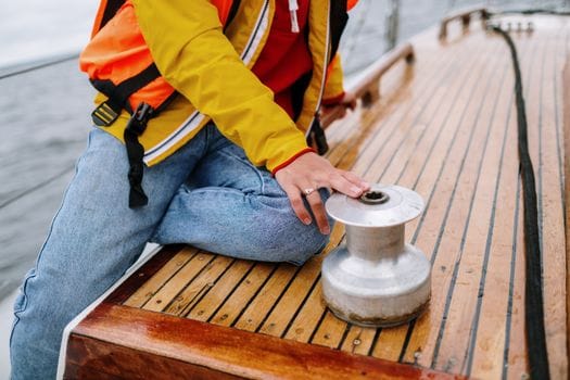 Cum să Alegi un Curs Maritim Distanță Acreditat: Tutorial Detaliat pentru Navigatorii Români 3 Close-up of a person operating a winch on a sailboat deck wearing a life jacket.