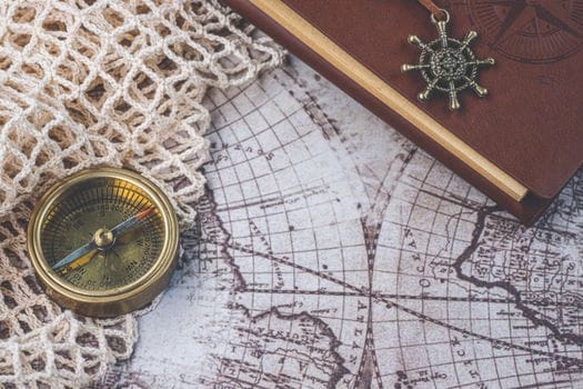 Cum să Compari Costurile pentru Certificatul STCW: Diferența Module 2010 vs 1995 2 Flat lay of a vintage compass and leather notebook on a retro maritime map.