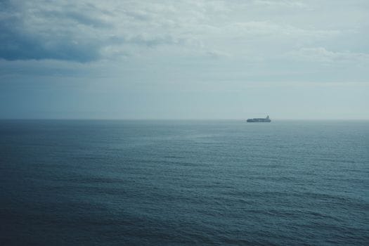 Cum să Completezi Cursul STCW Avansat Pompieri Maritimi: Cerințe și Pași Esențiali 2 A distant cargo ship navigates through the calm, expansive ocean beneath a cloudy sky, evoking solitude.
