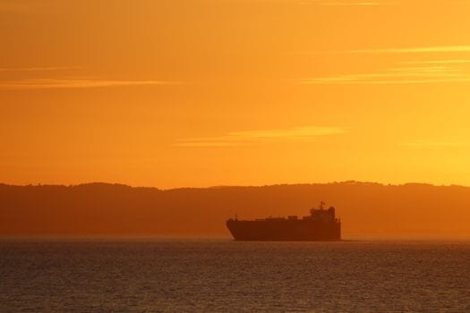 Cum să Crești Șansele de Angajare prin Curs Avansat Supraviețuire pe Mare Complet 4 A cargo ship silhouette against a dramatic orange sunset over calm waters.