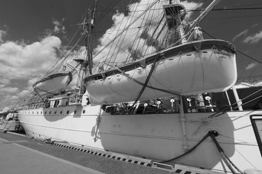 Cum să Îți Maximizezi Eficiența cu un Curs GMDSS Radiotelefonist Avansat în România 4 A majestic tall ship with lifeboats, docked under a vibrant sky on a sunny day.