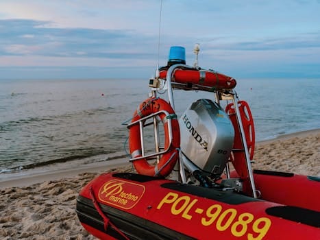 A red inflatable motorboat equipped with a Honda engine on a sandy beach at dawn.