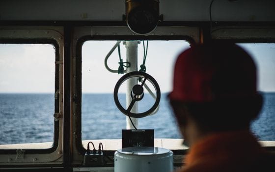 Cum să Profităm de Programul STCW pentru Navigatori Peste 50 Ani 2 Looking through a ship's bridge window towards the ocean horizon.