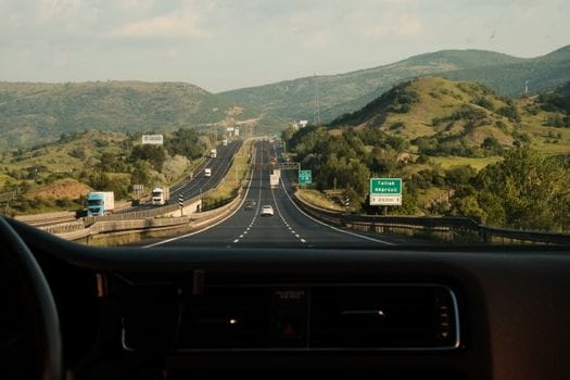 Cum să Tranzitionezi de la Curs Navigator Fluvial la Carieră Maritimă Globală 3 A scenic view of a highway through a car dashboard, surrounded by lush hills and clear skies.