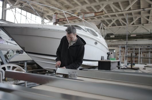 Cum să te Adaptezi la Certificatul STCW Manila: Actualizarea Cerințelor pentru Marinarii Români 3 Concentrated bearded adult workman in casual wear working with metal detail near boat in garage