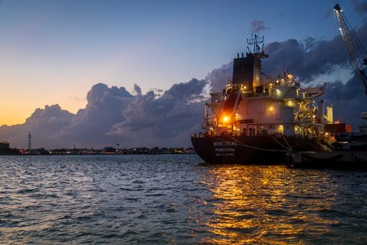 Pași pentru Obținerea Certificat STCW pentru Tanker Petrolier: Ghid Compleț 2 A cargo ship moored in a harbor during sunset, reflecting lights on the water.