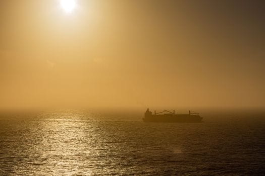 Pași pentru Obținerea Certificat STCW pentru Tanker Petrolier: Ghid Compleț 3 Silhouetted cargo ship navigating through misty ocean waters during sunrise.