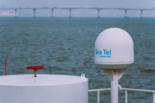 Pași pentru Pregătirea Eficientă la Examenul Radiotelefonist GMDSS: Cerințe și Beneficii pentru Navigatorii Români 4 A Sea Tel satellite antenna on a vessel with a bridge in the background over the ocean.
