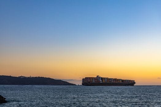Pași pentru Training Securitate Maritimă STCW București: Cum să Obții Certificatul 2 A cargo ship sails on the open sea against a colorful sunset sky, symbolizing global trade.