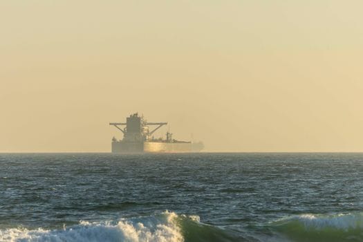 Pași pentru Training Securitate Maritimă STCW București: Cum să Obții Certificatul 3 A cargo ship silhouetted against the horizon on a calm ocean during twilight.