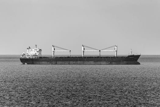 Pași pentru Training Securitate Maritimă STCW București: Cum să Obții Certificatul 4 Black and white photo of a bulk carrier traversing calm open sea under a clear sky.