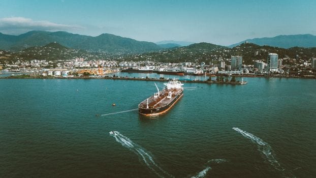 Adevărul despre Educatia Maritimă Online: De ce Nu Este Întotdeauna Răspunsul pentru Cariera ta pe Mare în România 2 Stunning aerial view of a large ship in the port of Batumi, Georgia, surrounded by lush mountains.