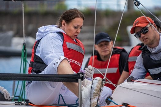 Group of adults sailing together in a boat wearing life jackets, focusing on teamwork and adventure.