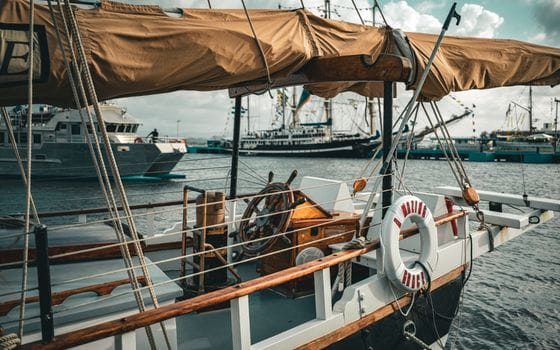 A rustic sailboat docked in a bustling maritime harbor, showcasing nautical charm.