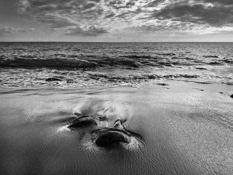 Cum să alegi corect cursurile STCW pentru o carieră de succes pe mare 4 Calm ocean waves meet the sandy shore in a black and white beach scene.