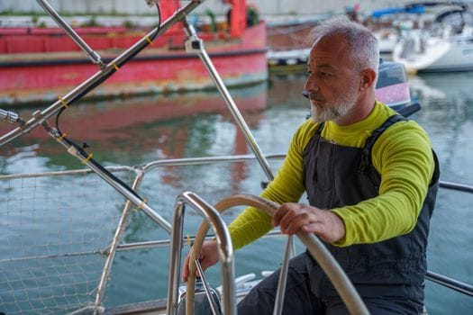 An experienced man steers a boat, focusing intently on the calm waterfront surroundings.