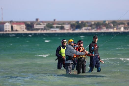 Ghid complet pentru obținerea certificatelor STCW necesare în cariera maritimă 4 A group of people receiving a kiteboarding lesson in shallow sea waters, equipped with helmets and gear.