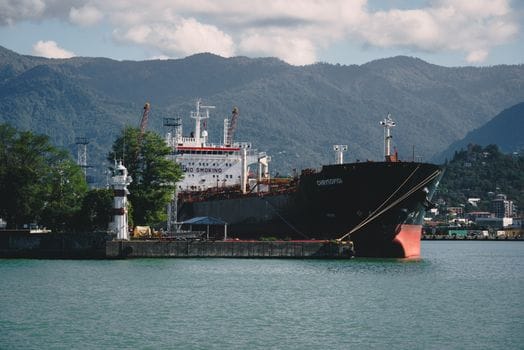 Pași esențiali pentru obținerea certificatelor STCW: ghid complet 4 A large cargo ship docks at a picturesque port with mountains in the background, highlighting maritime transport.