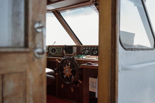 Pașii esențiali pentru obținerea certificatului STCW 2 A detailed view of a vintage boat helm featuring a wooden steering wheel and control panels.