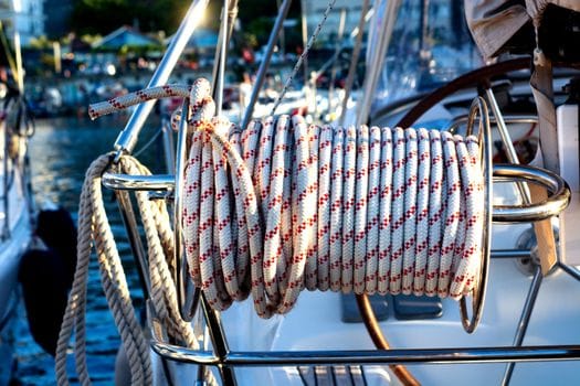 A vibrant close-up of a coiled sailing rope on a yacht, set against a sunny marina backdrop.