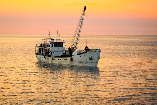 Top 5 Cursuri Maritime și Certificate STCW de Urmărit în România în 2026 2 A tranquil evening view of a cargo ship sailing during a vibrant sunset over a calm sea.