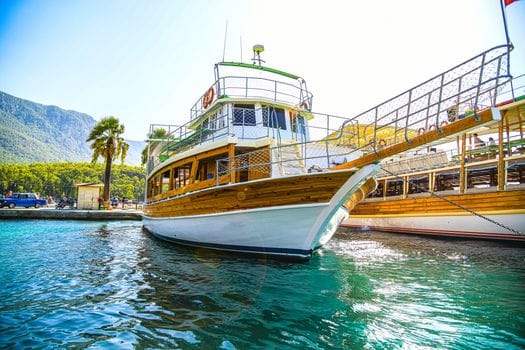 Top 5 Cursuri Maritime și Certificate STCW de Urmărit în România în 2026 3 A luxury yacht moored at a scenic dock in Akyaka, surrounded by palm trees and mountains.