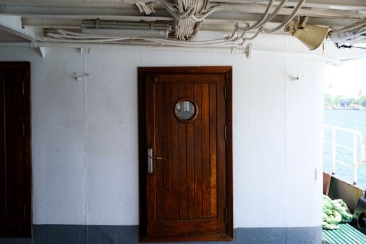 Training Maritim Avansat vs Cursurile de Bază STCW: Ce Alegi pentru Cariera ta în Vară 2026? 4 Close-up of a wooden door with porthole on a vessel deck, offering a nautical theme.