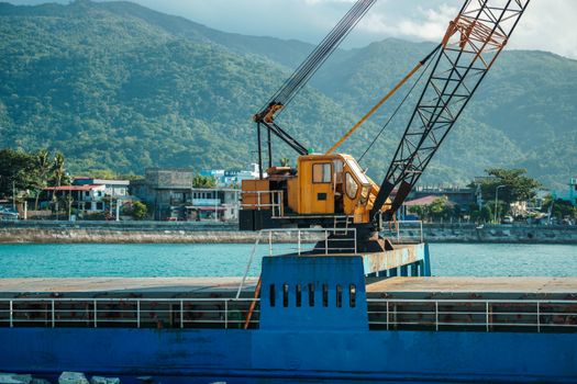 A vibrant industrial crane by the waterfront with a scenic mountain backdrop.