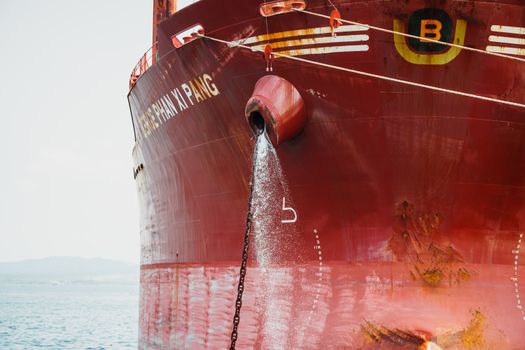 A large red cargo ship releasing water into the ocean. Visible markings and text on the ship's hull.